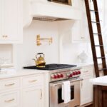 anne-wagoner-interiors-classic-white-kitchen-brass-accents-wolf-range-built-in-ladder-antique-artwork-above-hood-pot-filler