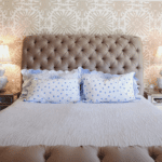 quadrille-Sigourney-wallpaper-bedroom-taupe-beige-camel-tufted-headboard-donghia-d-porthault-linens-mirrored-nightstands-hollywood-regency